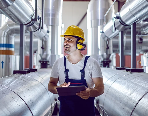 Industriearbeiter mit gelbem Helm und Tablet in einer Anlage zur Wartung und Inspektion.