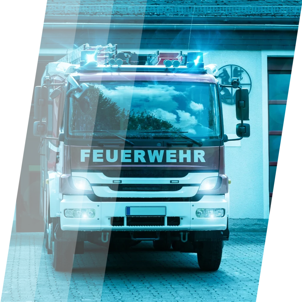 Feuerwehrfahrzeug mit eingeschaltetem Blaulicht vor einer Feuerwehrstation.