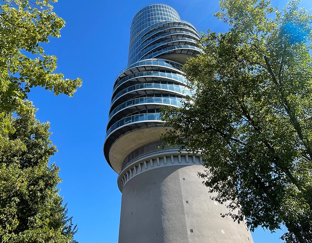 Modernes, rundes Bürogebäude in der Sonne, umgeben von Bäumen.