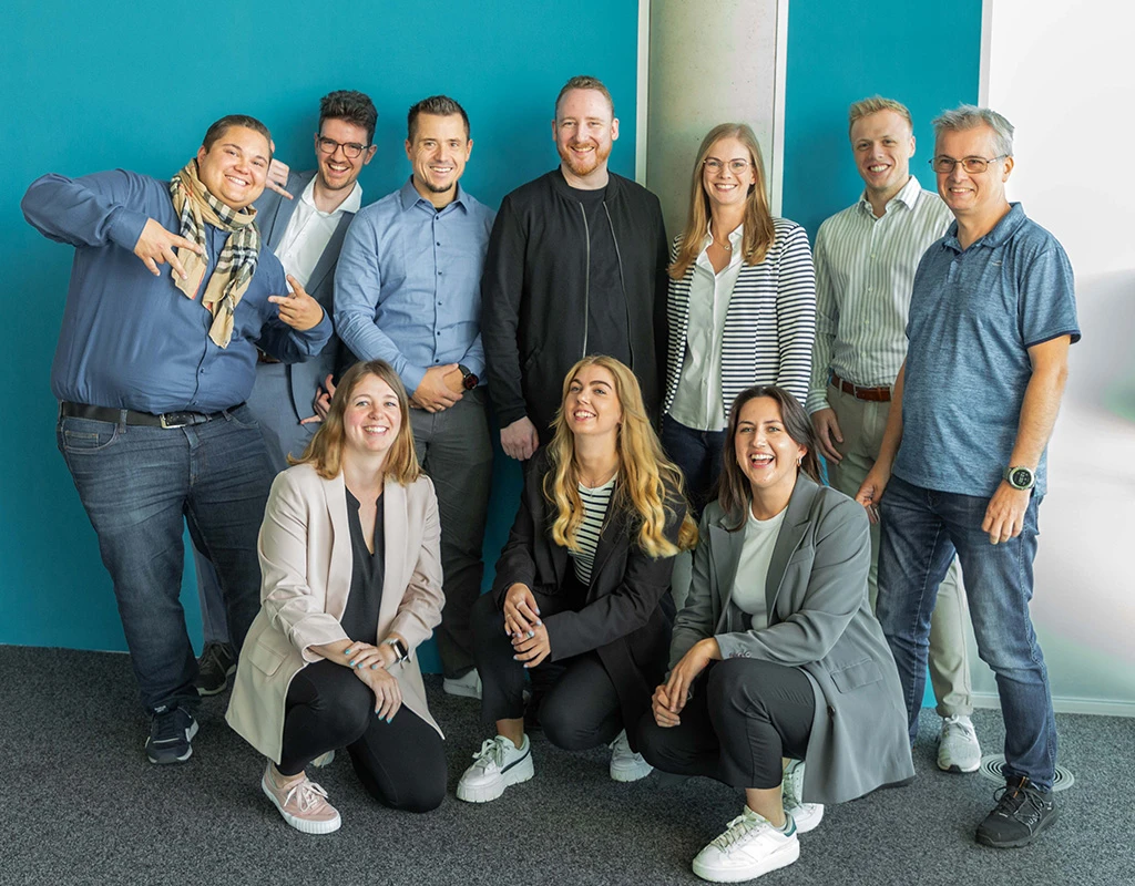 Das gesamte KEVOX-Team in einem Gruppenfoto vor einer blauen Wand.