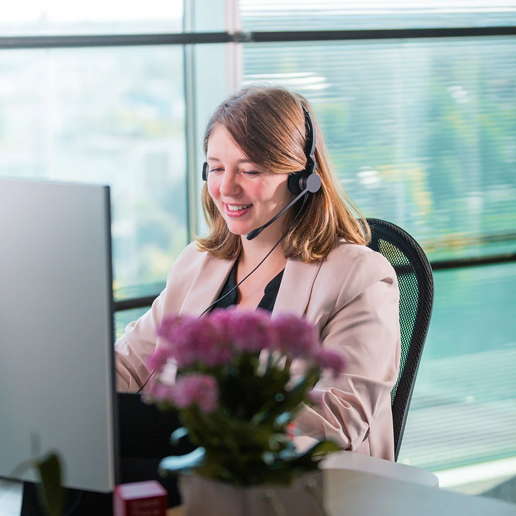 Freundliche Mitarbeiterin mit Headset am Computer im Kundenservice.