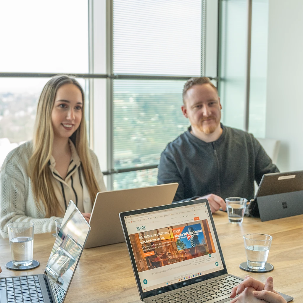 Teammitglieder bei einer Besprechung im Konferenzraum mit Laptops.