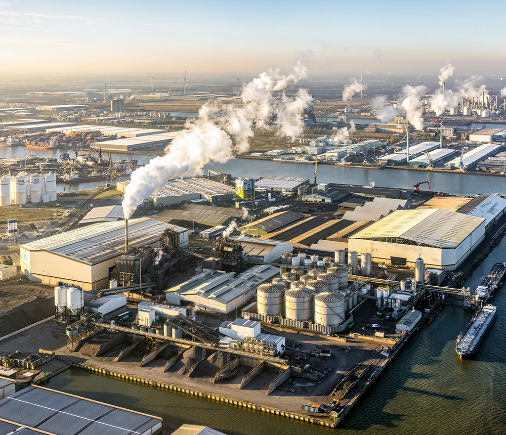 Luftaufnahme eines großen Industriekomplexes mit Schornsteinen und Fabrikhallen an einem Wasserkanal.