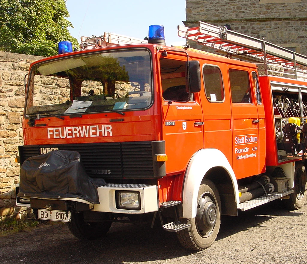 Feuerwehrauto der Stadt Bochum, parkt in der Nähe einer Steinmauer bei Tageslicht.