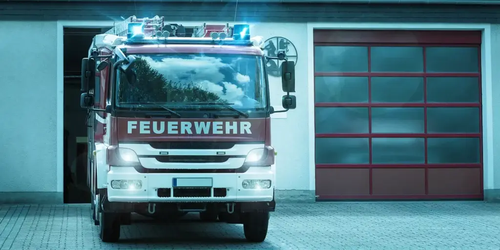 Feuerwehrfahrzeug mit eingeschaltetem Blaulicht vor einer Feuerwehrstation.